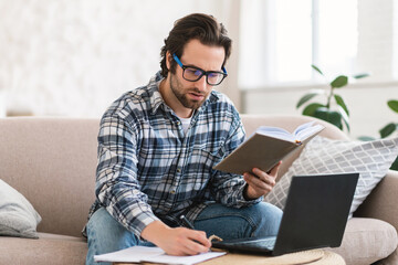 Busy smart millennial european male student in domestic clothes with stubble in glasses with book...
