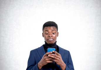 African businessman with phone, confused look on copy space concrete background
