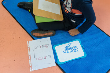 A young boy in a nursery school carries out an exercise of drawing a cat on a slate and a sheet of...