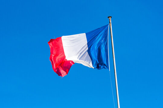The tricolor french flag (blue, white, red) in the wind with a blue sky