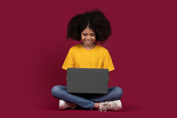 Fototapeta na wymiar Cheerful black girl schooler using laptop, colorful background