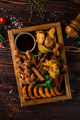 Beer set for party: onion rings, croutons, potato wedges, chicken legs and sauce on a wooden table.