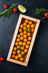 Deep-fried mashed potato croquettes served with green peas on a dark table.