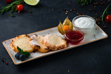 Breakfast cheese pancakes with jam, sour cream, blueberries and physalis on a plate.