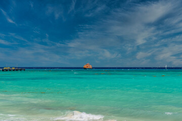 Fototapeta na wymiar Orange ferry in azure ocean with swimming people in Playa del Carmen, Yukatan, Mexico