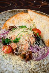 Lunch fried salmon fish with cheese, tomatoes, sun-dried tomatoes, olives, onions, greens and toast.