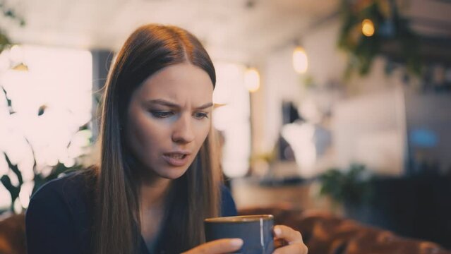 Young woman trying too hot coffee, breakfast in cafeteria, cafe visitor