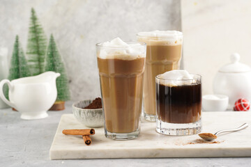 Three tall glasses with warm coffee drink with cinnamon, whipped milk foam and caramel on a marble board and christmas ornaments and decoration
