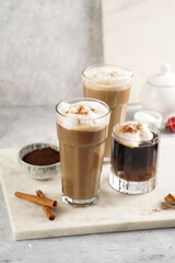 Obraz na płótnie Canvas Three tall glasses with warm coffee drink with cinnamon, whipped milk foam and caramel on a marble board and christmas ornaments and decoration