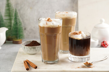 Three tall glasses with warm coffee drink with cinnamon, whipped milk foam and caramel on a marble board and christmas ornaments and decoration