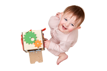 Happy toddler baby boy is playing with a busyboard cube on the nursery floor, isolated on a white background. Educational toys for children, wooden game pane. A child aged one year