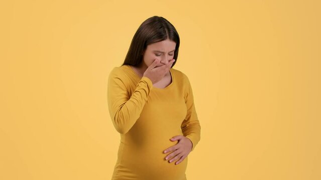 Pregnancy and toxicosis. Young upset pregnant lady feeling unwell, suffering from nausea, yellow background, free space