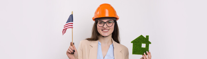A girl in a construction helmet and an American flag holds a green eco house.