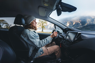 Young smiling caucasian woman driver traveler in a hat and jacket driving a car while traveling...
