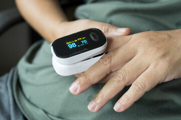Woman resting at home using pulse oximeter to monitor blood oxygen levels and pulse rate. finger inserted into the pressure oximeter to assess health from the living room home. - obrazy, fototapety, plakaty