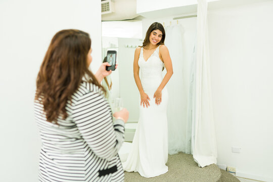 Friend taking a picture of a future bride while trying a wedding dress in a shop