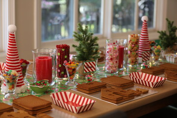 Christmas gingerbread house decorating party set up on decorated table with candy, candles and Christmas tree