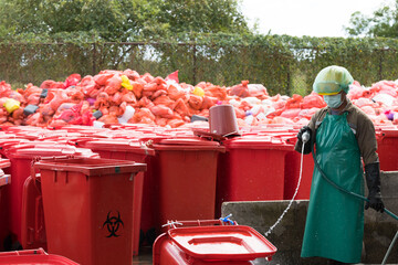 Workers cleaning infected bins for destruction in a waste disposal facility.Big red garbage jugs on...
