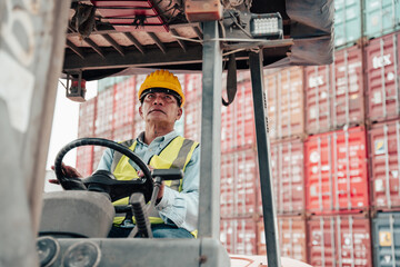 Male worker wearing a helmet drives a forklift inspecting containers.