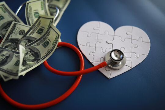 A stethoscope on money and a puzzle heart. Health insurance. Healthcare and medicine. How much is the treatment. Money and medicine. World Heart Day. World Health Day. 