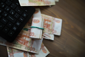 Stacks of 5000 ruble banknotes on the table next to the laptop. Savings and investments in the conditions of sanctions and inflation.