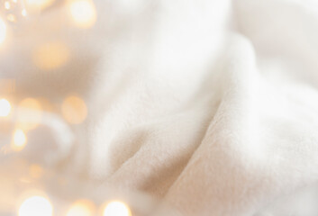 Atmospheric background with detail of a fluffy, comfortable fabric blanket and twinkling lights. Cosy winter, Christmas concept. - obrazy, fototapety, plakaty