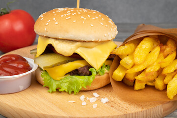 Hamburger with tomatoes, pickles and cheese. Nearby is a portion of french fries