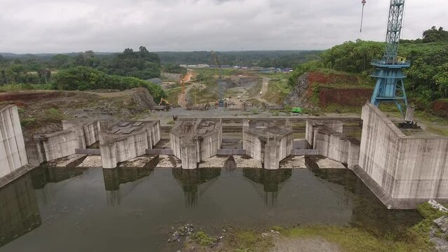 Aerial view. The construction of a hydroelectric dam in the tropical jungle. Construction cranes at the dam on the river. Equatorial Guinea, Africa.