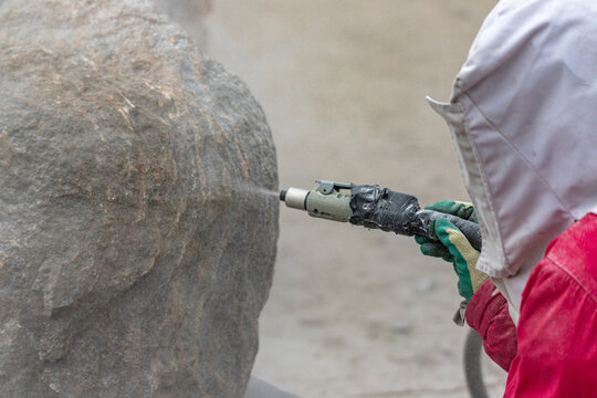 Cleaning Granite Boulder Rock Surface With Sand Blasting Method. Browing Sand With High Air Pressure