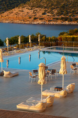 Luxury morning swimming pool with empty deck chairs, tables and umbrellas at the resort with...