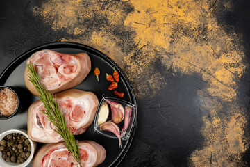 Seasoned pork knuckles on a plate with spices on an abstract background of a meat table, copy space - obrazy, fototapety, plakaty