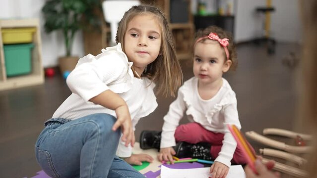 Two little girls drawing on notebook sitting on floor at kindergarten