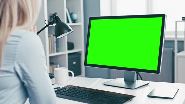 Woman in formal clothes talking from office using video call on computer, chromakey green screen ready for copy space of conversation partners