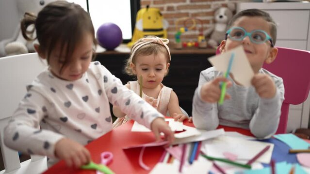 Group of girls and boys sitting on table cutting paper at kindergarten