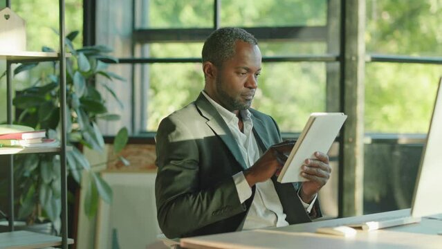 Close Up Handsome African American Man With A Beard Working Use Tablet Computer Look At The Camera At Sunlight In Office Technology Businessman. Worker. Slow Motion