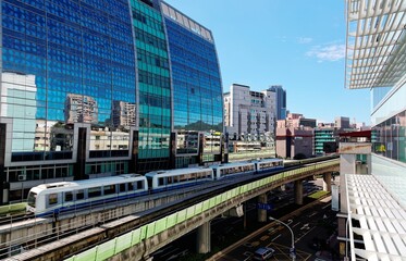 Fototapeta na wymiar View of a train traveling on elevated rails of Taipei Metro System by a modern building of glass curtain walls on a beautiful sunny day ~ View of MRT railways in Taipei, the capital city of Taiwan