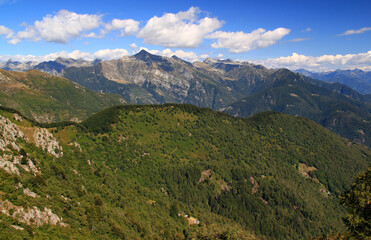 Fototapeta na wymiar Panoramic view of the landscape with mountains and green hills in the foreground against a blue sky with clouds on Mount Cimetta, near Locarno in Switzerland