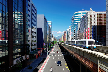 Fototapeta premium A metro train traveling on the elevated rail of Taipei MRT between office towers under blue sky ~ View of a public transportation system in Taipei, the capital city of Taiwan, on a beautiful sunny day