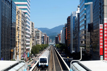 A metro train travels on elevated tracks of Wenhu Line of Taipei Metro System by office towers under blue clear sky ~ View of MRT railways in Taipei, capital city of Taiwan, on a beautiful sunny day