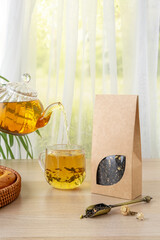 Organic tea branding and packaging mockup. Jasmine green tea in glass teapot on table. Hot tea is...