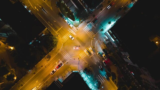 Crossroad traffic aerial drone video time lapse from above at night, topdown fly footage above cars in an intersection