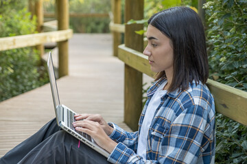 Girl typing on laptop in the field sitting on the ground