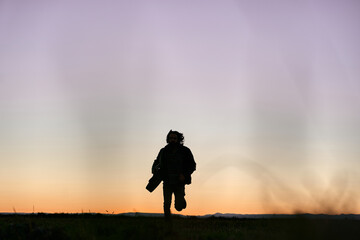 silhouette of caucasian guy in fur jacket running towards camera next to his guitar at sunset