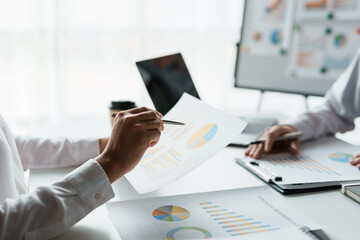 Two business people point to graphs and charts to analyze market data, balance sheet, account, net profit to plan new sales strategies to increase production capacity.