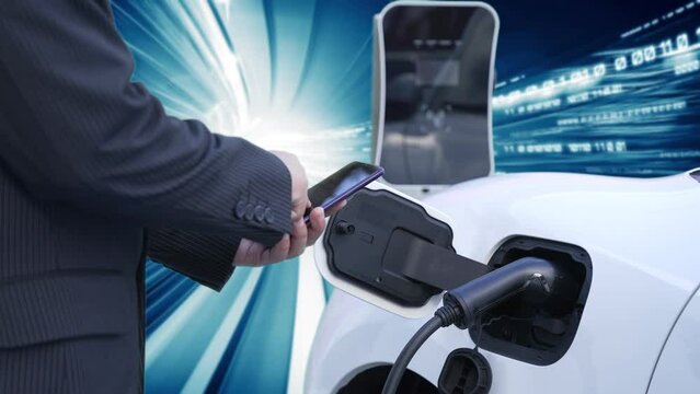 Progressive man check electric car's battery status with smartphone at charging station with technology background of binary code flying through votex. EV car concept with modern technology.