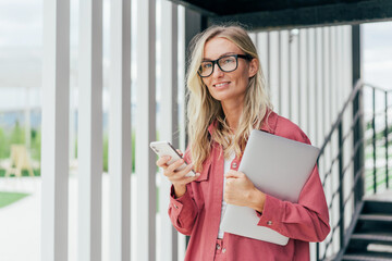 Happy blond business woman in pink jacket holding laptop computer