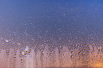 condensation from a drop of water on a window glass pane during dawn with orange and blue tones