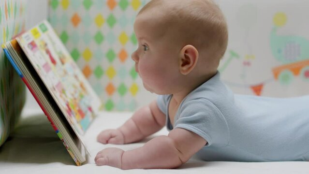 Baby and book. The child looks very carefully at the picture book while lying in his bright bed. The concept of child development, education, intelligence, science. Slow motion.
