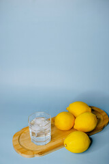 yellow lemons lie on a wooden board with a glass of water on a blue background