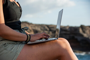 Caucasian girl by the ocean working with her laptop, freelance work concept.